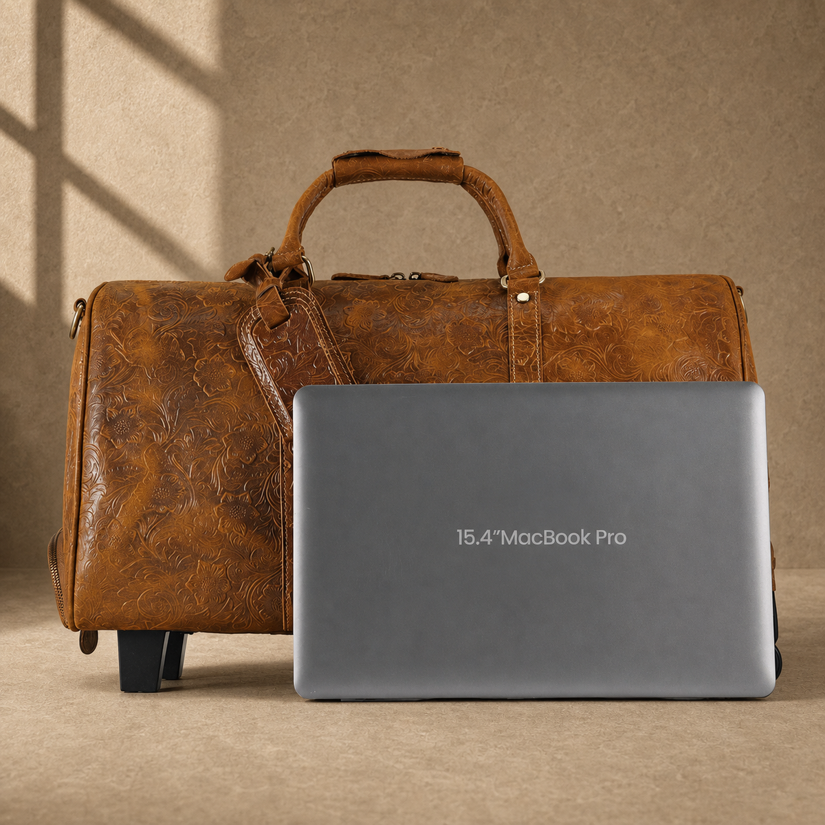 Cognac floral rolling duffle shown beside a 15.4-inch laptop