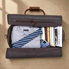 Open cognac rolling garment bag packed with shirt, tie, books and phone